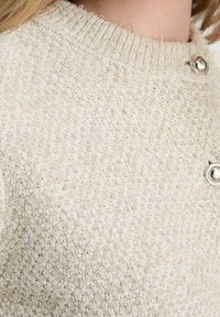 Vaaleanbeige neulottu neuletakki, jossa on teksturoitu pinta, pyöreä pääntie ja hopeanväriset napit.