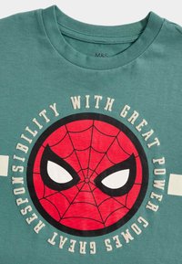 Green cotton t-shirt with a red Spider-Man graphic at the center, featuring a webbed design and white text around the circle.