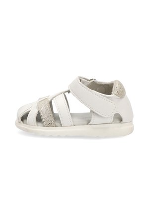 Sandalia blanca para niño pequeño con múltiples tiras, una brillante, una tira de velcro en el tobillo y suela acolchada, vista lateral sobre fondo blanco.