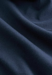 Granatowa bawełniana tkanina o gładkiej fakturze, z subtelnym prążkowaniem i delikatnymi fałdami, podkreślająca swoje miękkie i elastyczne właściwości.