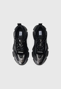 Mustat lenkkitossut, joissa on matta- ja kiiltäväpintaisia osia. Niissä on paksut pohjat, verkkokuviointia sekä metallinhohtoiset yksityiskohdat kärjessä ja sivuilla.