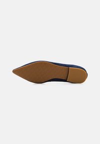Sapatilha de bico fino azul-marinho com parte superior em tecido texturizado. A sola é de borracha castanha com um design de padrão na sola, proporcionando aderência e durabilidade.