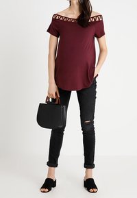 Mörkröd off-shoulder topp med utskärningsmönster, ihopparad med svarta skinny jeans med ett rivet knä, svart handväska och svarta slides.