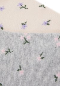 Knästrumpor med blommönster. Ena sidan är krämig med lila blommor, den andra är grå med rosa och gröna detaljer, ribbat mönster.