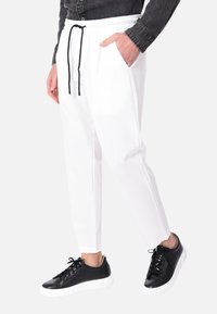 Pantaloni bianchi con vita a coulisse, tasche laterali e una vestibilità rilassata, abbinati a sneaker nere con suola bianca.