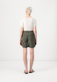 Shorts verts à coupe droite, avec des poches latérales et des poches passepoilées à l'arrière, associés à un top blanc texturé à manches courtes.