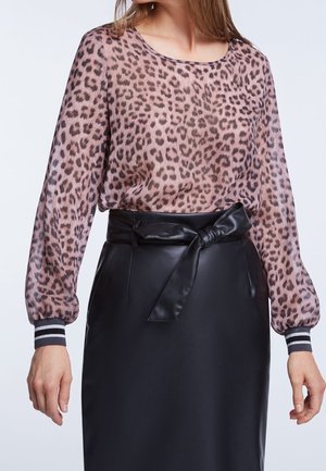 Kvinde iført en langærmet lyserød og brun leopardmønstret bluse, stukket ned i et sort lædernederdel med højtaljet, med et knyttet bælte i taljen.
