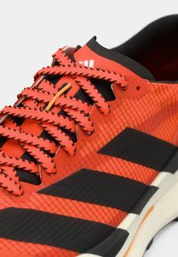 Κόκκινο αθλητικό παπούτσι με επάνω μέρος από δίχτυ, μαύρες λεπτομέρειες και αντίθετους μαύρους κορδόνια. Διαθέτει υφή στο σχέδιο και μαλακή σόλα.