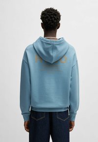Felpa blu con un grande logo dorato e testo sul retro, dotata di cappuccio con cordino e polsini a costine, realizzata in tessuto morbido.