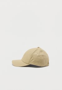 Casquette de baseball beige avec une visière incurvée, fabriquée en tissu texturé. Présente un motif de logo subtil et des trous d'aération sur la couronne.