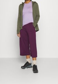 Olivgrön zip-up hoodie, lila åtsittande t-shirt, lila culottes och svarta sportskor med ljusgrå accenter och krämfärgade strumpor.