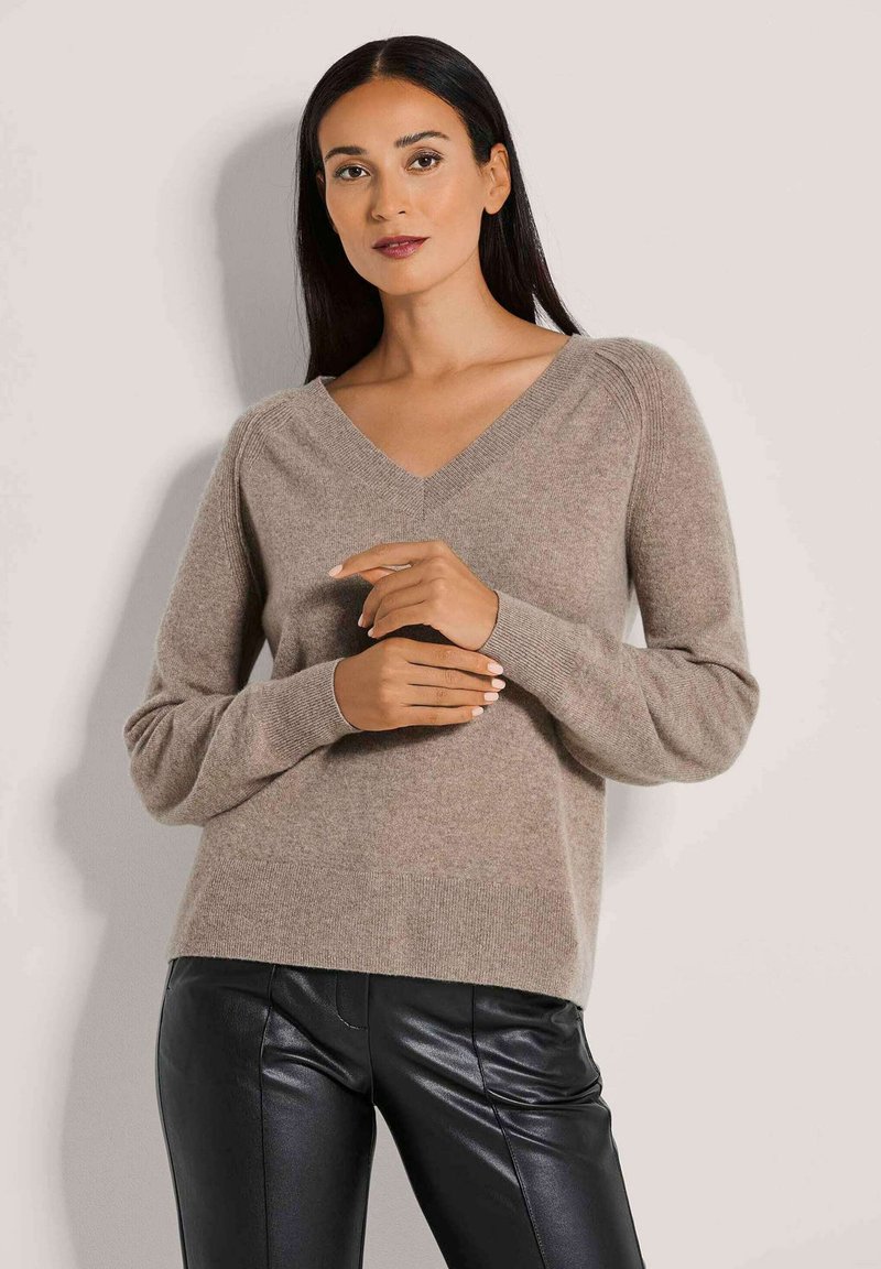 Beiger V-Ausschnitt-Pullover aus weichem Material mit langen Ärmeln, gerippten Bündchen und lockerer Passform, kombiniert mit schwarzen Lederhosen.