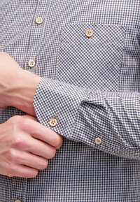 Camicia button-up con motivo a quadri blu e bianchi, in materiale cotone, colletto a punta e quattro bottoni chiari sul polsino e sulla tasca.