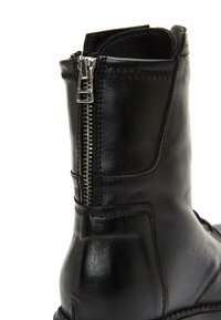 Bottine noire en cuir avec une fermeture éclair latérale, une texture lisse et des coutures renforcées pour une meilleure durabilité.