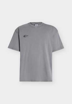 T-shirt grigia a maniche corte con piccolo logo nero "ARKK" sul petto in alto a sinistra e scollo rotondo.