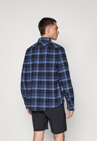 Blue and black plaid shirt with red and white accents, button-down collar, fabric texture visible, paired with black shorts.