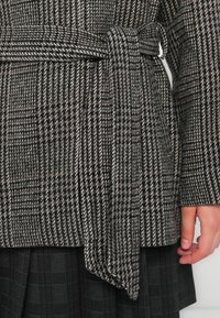 Wool-blend plaid coat in gray and black, featuring a belted waist and textured fabric with a houndstooth pattern.