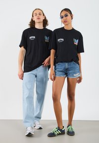 Black t-shirts with butterfly embroidery on the chest, paired with light blue jeans and denim shorts. Footwear includes athletic sneakers.