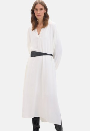 Abito bianco a maniche lunghe con scollatura a V, stretto in vita da una cintura nera. Tessuto morbido con silhouette fluida, abbinato a leggings a contrasto.