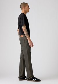 Zwarte T-shirt gecombineerd met olijfgroene jeans, met een rechte pasvorm, klassiek vijfzakdesign, en zwarte sneakers met witte strepen.
