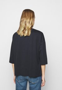 Schwarzes, oversized T-Shirt mit Rundhalsausschnitt und Dreiviertelärmeln, aus einem weichen Baumwoll-Mix gefertigt. Glatte Textur und lockere Passform.