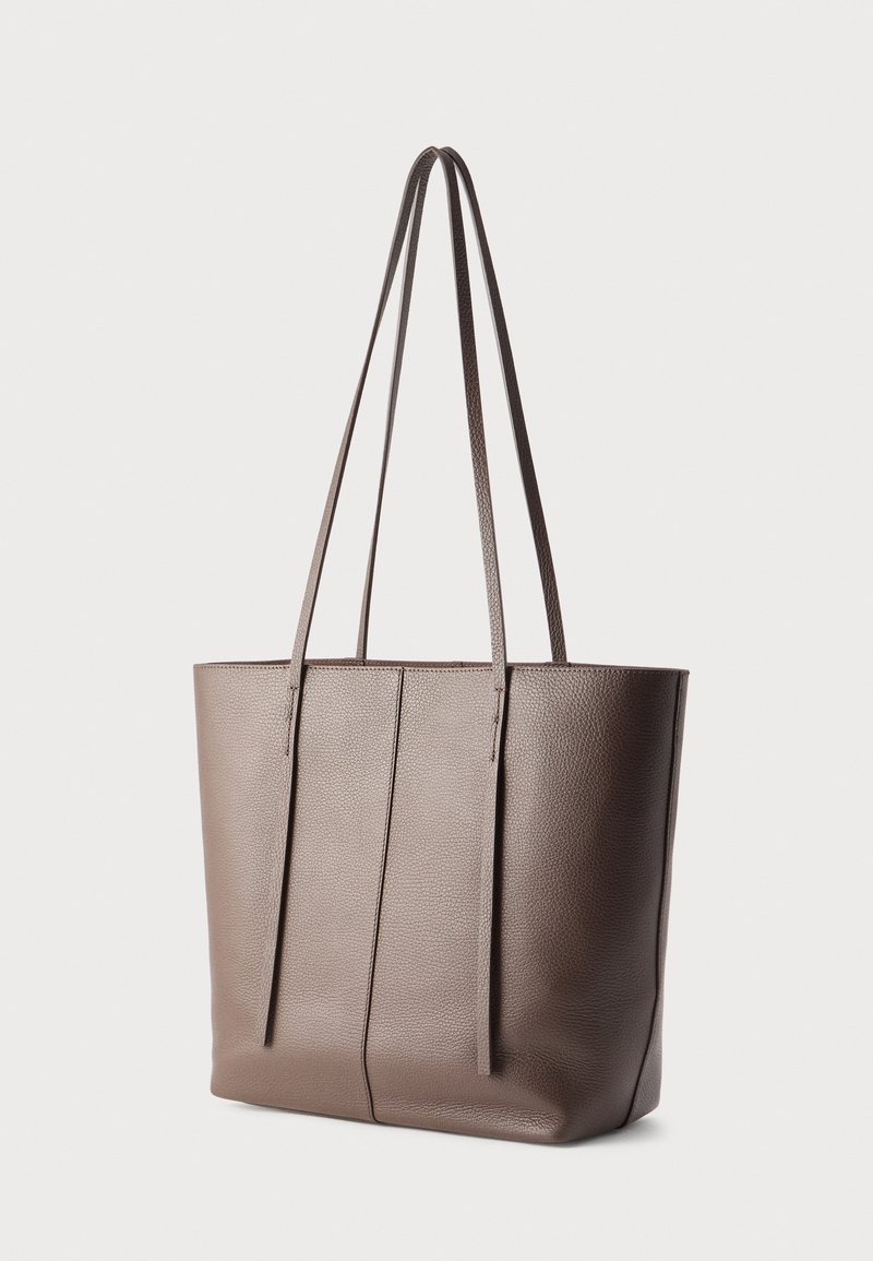 Sac fourre-tout en cuir marron avec deux longues anses, une texture lisse, un corps large et des détails de coutures verticales sur le devant.