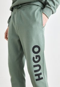Grønne bomullsblandede joggebukser har elastisk midje, sidelommer og en stor svart "HUGO"-logo på venstre ben.
