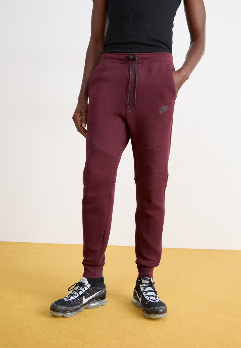 Bordo Nike trenirke s pojasom na vezanje, suženim nogavicama i kontrastnim šavovima. Imaju logo na bokovima i elegantnu, meku teksturu tkanine.