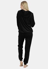 Black fleece loungewear set featuring a hooded top with long sleeves and matching pants with elastic cuffs, designed for comfort.