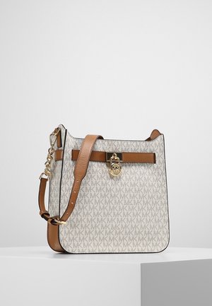 Sac à bandoulière beige monogrammé Michael Kors avec bandoulière en cuir marron et détail de serrure dorée à l'avant.