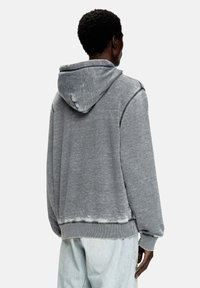 Sweat à capuche gris avec une texture délavée, des poignets et un ourlet côtelés, et un détail de couture visible le long du dos.