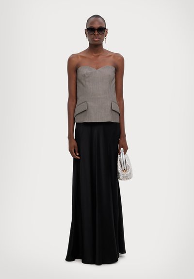 Grijze strapless top met een sweetheart halslijn en zijzakken, gecombineerd met een lange zwarte satijnen rok. Houdt een zilveren handtas vast.