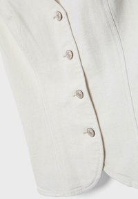 Detail bielej rifľoviny s vertikálnym švom a štyrmi striebornými patentkami zoradenými v rade.