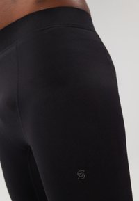 Leggings atléticos pretos com uma textura suave, cintura elástica e um detalhe sutil do logo na perna inferior. Design ajustado.