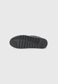 Schwarze Sneakersohle aus strukturiertem Gummi mit horizontalen und vertikalen Rillen sowie einem Logodetail in der Nähe der Ferse.