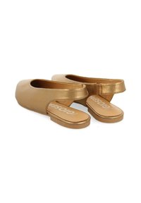 Zapatos dorados sin cordones con un acabado metálico suave, sin parte trasera, y una suela plana. Presentan un sutil logotipo de la marca en la plantilla.