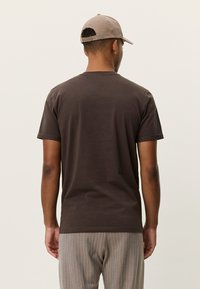 Μαύρο-καφέ βαμβακερό μπλουζάκι με κοντά μανίκια, στρογγυλή λαιμόκοψη και διακριτική υφή, συνδυασμένο με ανοιχτό γκρι ριγέ παντελόνια. Πλάγια όψη από πίσω.