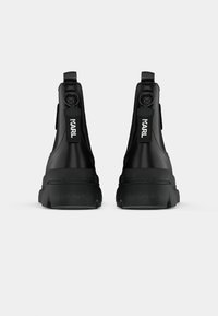 Botas ankle pretas com um acabamento suave, apresentando uma sola resistente, abas para puxar na parte traseira e o nome da marca "KARL" nas tiras traseiras.