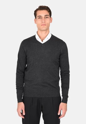 Maglione grigio scuro a maglia con scollo a V, maniche lunghe e polsini a coste. Abbinato a una camicia bianca con colletto sotto.