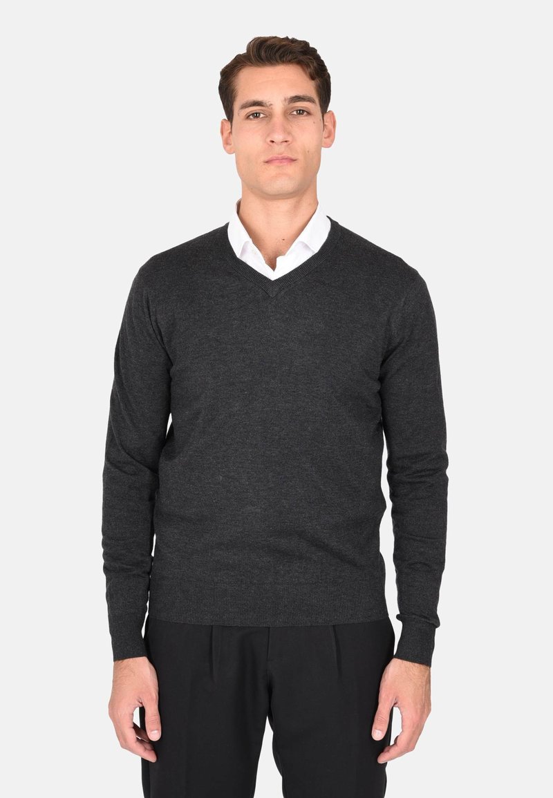 Maglione grigio scuro a maglia con scollo a V, maniche lunghe e polsini a coste. Abbinato a una camicia bianca con colletto sotto.