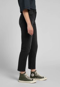 Black denim jeans with a tapered fit, five-pocket design, and cuffed hems, paired with green high-top sneakers with white accents.