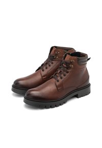 Botas de tobillo de cuero marrón con un acabado texturizado, puntera redonda y suela de goma negra contrastante. Cuenta con cordones y ojales metálicos.