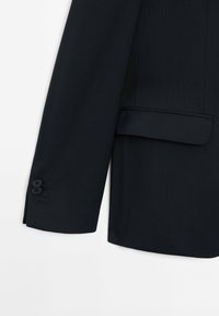 Marineblauer Nadelstreifenblazer mit aufgeschlagenem Revers, einer Brusttasche und zwei schwarzen Knöpfen am Ärmel. Glatte Textur und strukturierte Passform.