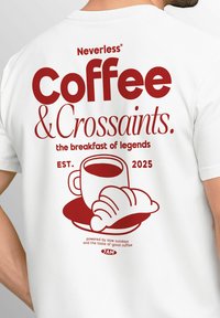 Weißes T-Shirt mit auffälligem roten Text "Neverless Coffee & Croissants." Grafik einer Tasse Kaffee und einem Croissant, mit "EST. 2025."