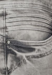 Šedá džínová látka s vybledlou texturou, s prošívanou zadní kapsou a stříbrnými kovovými detaily.