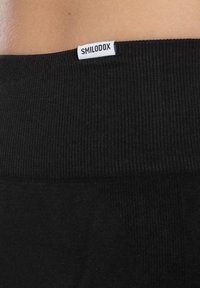 Zwarte geribbelde tailleband met een wit "SMILODOX" label. De stof lijkt zacht met een gladde textuur, geschikt voor sportkleding.