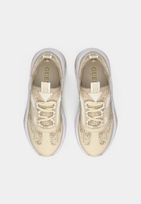 Baskets beiges avec une tige en maille à motif, dotées d'accents blancs, d'un design à lacets et d'une semelle translucide. Détail de logo doré visible.