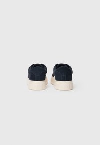 Tumedat sinised suede ketsid valge kummitaldiga, pehme tekstuuriga, ümarate kontsadega ja tagaküljel embosseeritud logoga.