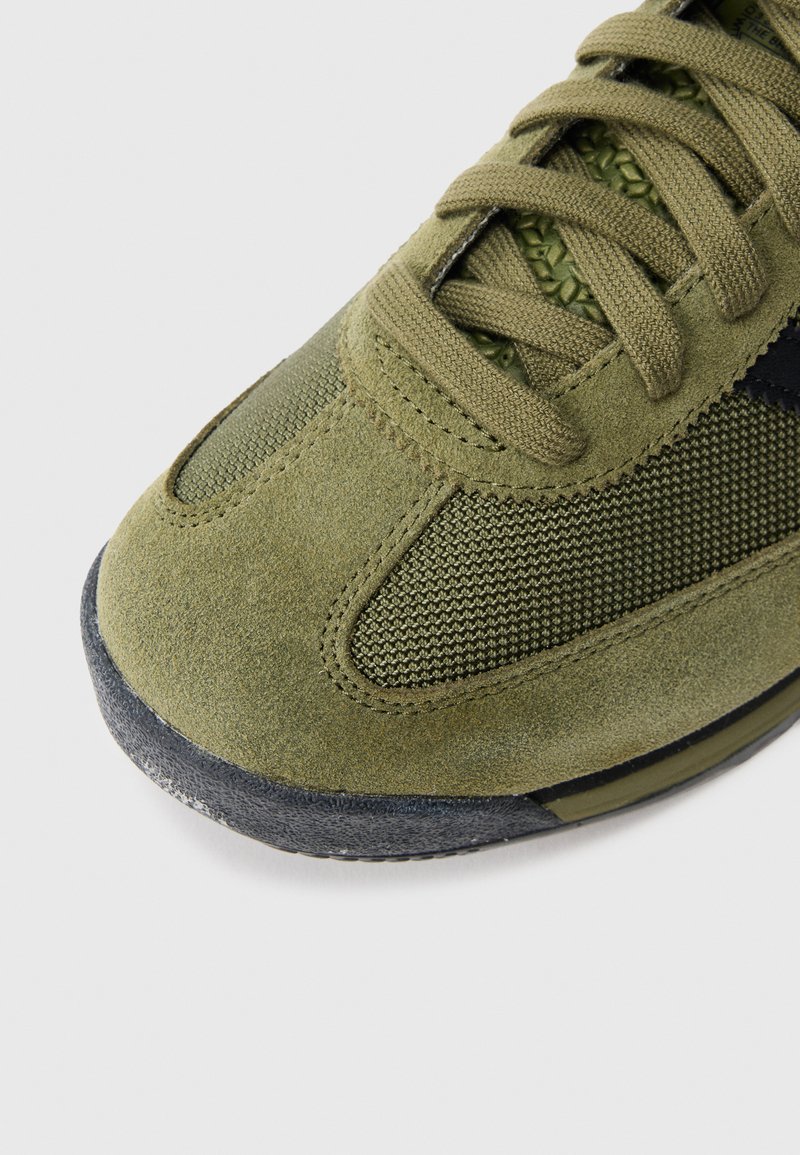 Sneaker in suede verde e mesh con punta rotonda, tomaia texturizzata e dettagli neri. Presenta lacci, cuciture visibili e suola in gomma.