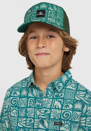 Casquette de camionneur verte avec un devant à motifs comprenant des feuilles et des designs géométriques ; chemise assortie couleur sarcelle avec des motifs similaires et un col boutonné.